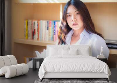 Young asian woman at home sitting in front of book shelf relaxing in her living room reading book Wall mural