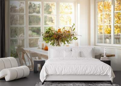 A dining room with a light wooden table, white chairs, and a centerpiece of autumn foliage and candles Wall mural