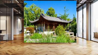 Scenic view of a beautiful Chinese temple building in the Chinese Garden in the city of Stuttgart, Germany under a clear blue sky. Bushes and plants surround this peaceful spot. Wall mural