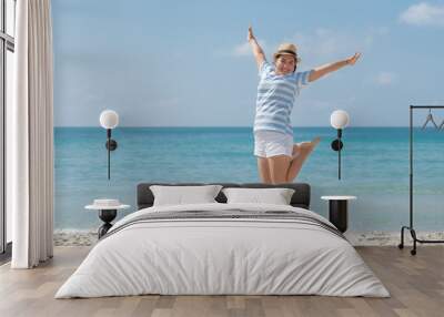 Asian young woman wearing a hat is jumping with enjoy and happiness on the beach. Wall mural