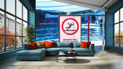 BEWARE FALL TO THE WATER plastic future board sign on traffic barrier with wheels outdoor pool is background. Wet Floor sign white rectangular shape with falling man. Caution warning beware danger.  Wall mural