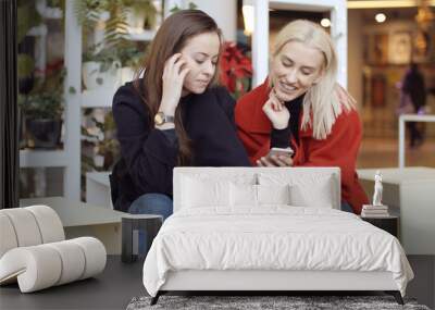 Two young girls using mobile phone in a city. Wall mural