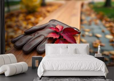 A pair of worn leather gloves lie on a smooth, polished wooden bench, their surfaces catching the subtle reflections of nearby golden and crimson leaves.  Wall mural