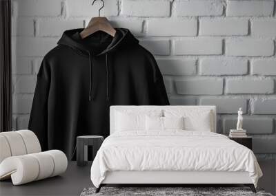 A plain black hoodie hanging on a wooden hanger against a white brick wall. Wall mural