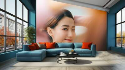 Beautiful asian woman tying hair looking at mirror. Wall mural