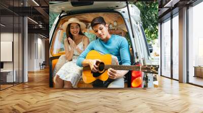 Couple playing guitar at car trunk in camping area. Wall mural