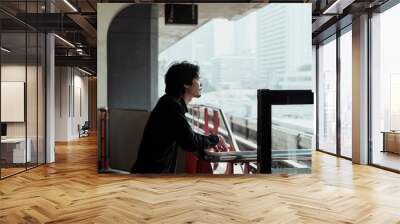 Side view of a man looking at city on sky train platform. Wall mural