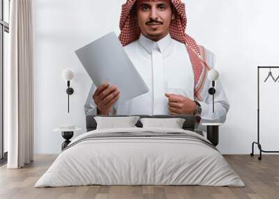 Reviewing and following up on office plans and projects, a portrait of a Saudi Gulf Arab man wearing a traditional thobe and shemagh and holding a group of white papers in his hand, preparing work rep Wall mural