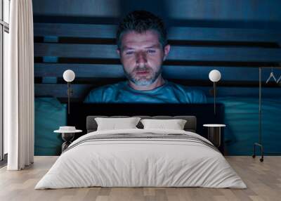 attractive and relaxed internet addict man networking concentrated late at night on bed with laptop computer in social media addiction or workaholic businessman concept Wall mural