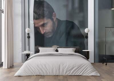 dramatic portrait of attractive sad and depressed mid adult man looking through home window feeling worried and desperate suffering depression problem thoughtful in pain Wall mural