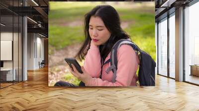 happy Asian woman using mobile phone at city park - young sweet and beautiful Korean girl sitting on green grass networking enjoying social media with hand phone Wall mural