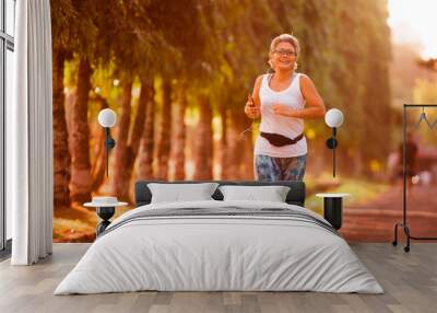 middle aged 40s or 50s happy and attractive woman with grey hair training at city park with green trees on sunrise doing running and jogging workout in health care Wall mural