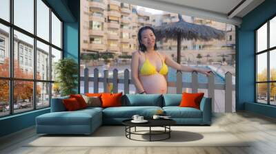 outdoors summer holidays portrait of young happy and attractive Asian Chinese woman pregnant at resort swimming pool enjoying carefree proud of her belly in maternity concept Wall mural