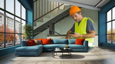 portrait of upset construction worker or stressed contractor man in hardhat and vest checking on mobile phone unhappy in stress messing with work problem Wall mural