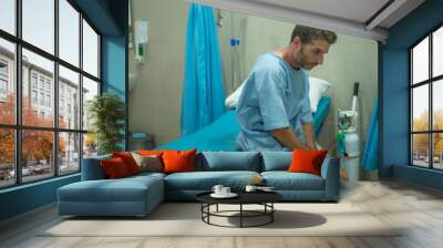 scared and worried man hospitalized - attractive injured man sitting on hospital bed receiving treatment feeling sick and unwell after suffering accident or serious disease Wall mural