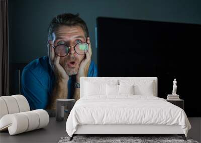 weird shocked and surprised geek man in nerd glasses working on laptop computer late night in the dark looking funny in shock and disbelief face expression Wall mural