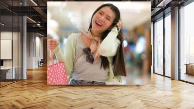 young beautiful Asian woman shopping at modern mall - happy and attractive Japanese girl holding shopping bags smiling excited enjoying sale buying at beauty fashion store Wall mural