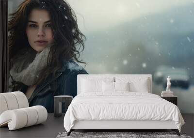 A young woman stands on a snow-covered road, her hair blowing in the wind as she gazes into the distance. Wall mural