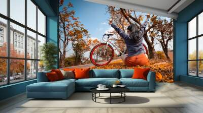 The back woman arms raised and sitting next to her bike outdoors at palash tree with full of beautiful orange flower background Wall mural