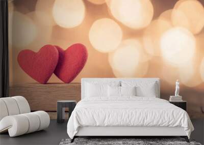 Two red hearts on a wooden surface with a golden bokeh background, symbolizing love and affection. Wall mural