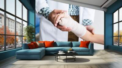 Close-up of man doctor of checking splint the arm of female patient hand due to with her arm broken for better healing with a smile sit in a wheelchair In the room hospital background. Wall mural