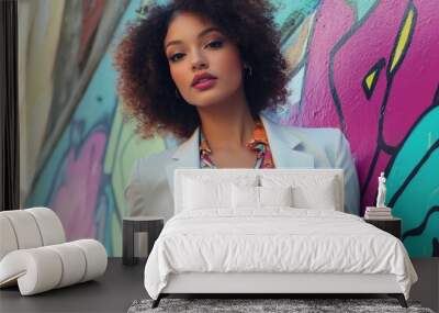 A confident woman in an elegant blazer and floral blouse stands against the backdrop of vibrant street art, her curly hair flowing gracefully as she poses for the camera with one hand on her hip Wall mural