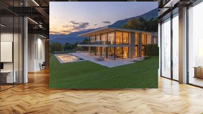 A contemporary, minimalist house in an Italian mountainous region with large windows and glass walls overlooking the green lawn, a white terrace on two floors, a swimming pool behind it Wall mural