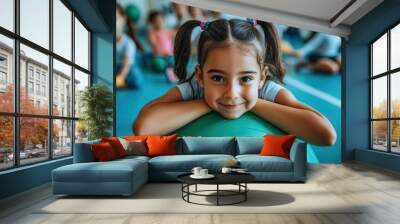 A happy little girl is sitting on a green fitness ball and playing with her friends in the children's gym at a nursery school. Wall mural