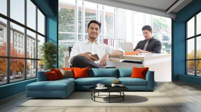 Happy young businessman sitting in the office. Business on mobile phone and computer. Laptop on the table. Wall mural