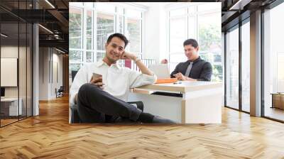 Happy young businessman sitting in the office. Business succes on mobile phone and computer. Mobile phone on hand. Wall mural