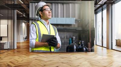 Male heavy industrial worker using a digital tablet inside manufacturing. Acetylene and oxygen gas steel storage tanks for welding. Wall mural