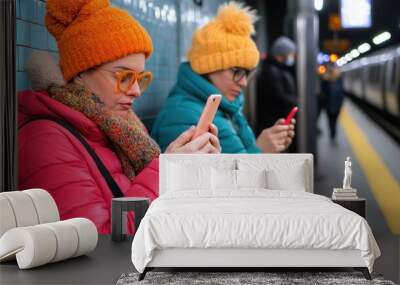 Two Women in Colorful Winter Clothing Using Smartphones on Subway Platform, Urban Commuters in Modern Public Transportation Setting Wall mural