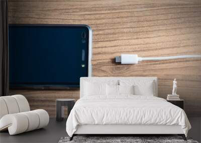 black smartphone and white cable connecting or charger on wood board Wall mural