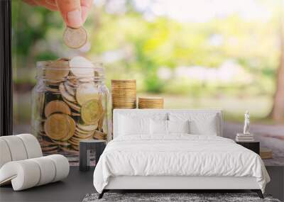 investor business man hand putting coins in jar on wood table with blur nature park background. money saving concept for financial banking and accounting. Wall mural