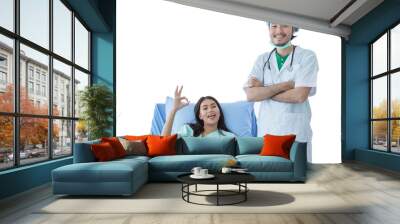 Positve good looking male doctor with white coat is smiling, standing near happy young female patient showing OK sign with hospital clothes on hospital bed, isolated white background. Wall mural