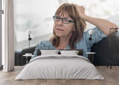 Pensive mature woman sitting on sofa Wall mural