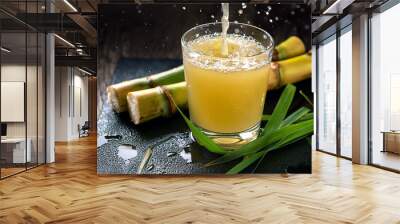 Refreshing sugarcane juice pouring into a glass, accompanied by stalks and leaves. A burst of natural sweetness! Wall mural