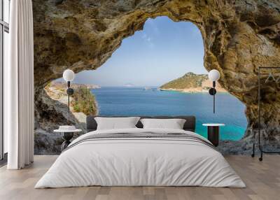 Beautiful sunny view through a rocky cave to the greek blue sea with crystal clear water from an a hill with boats cruising fishing surrounded by mountains, Patmos Island, Kos, Dodecanese/ Greece  Wall mural