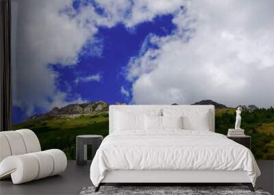 wonderful mountain with green places and white clouds on blue sky Wall mural