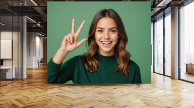 portrait of attractive amazed cheerful girl showing v-sign having fun isolated over green color background Wall mural