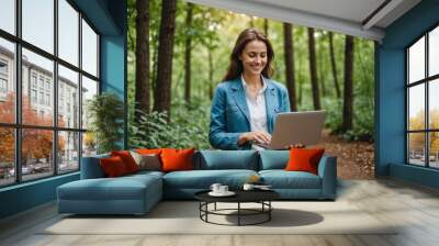 Smiling woman holding laptop using mobile phone in nature Wall mural