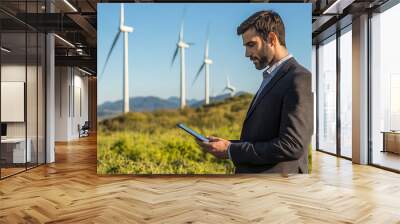 A wind farm site with a business professional in a suit examining a tablet, standing in front of large wind turbines under a clear blue sky, symbolizing corporate involvement in renewable energy  Wall mural