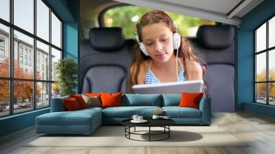 Technology, young girl in car with tablet and headphones while travelling. Social media or streaming, internet connectivity and child on road trip on vacation in vehicle with digital or mobile device Wall mural