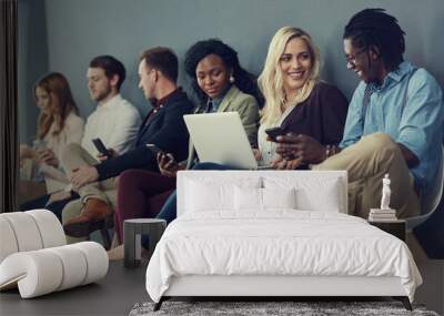 Youve been shortlisted but who will get the job. Shot of a group of businesspeople using different wireless devices while waiting in line for an interview. Wall mural