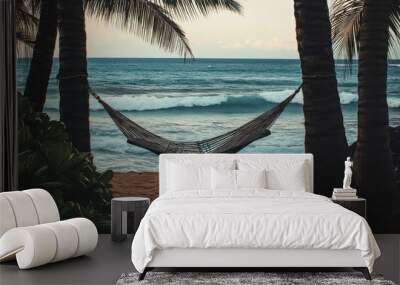 An empty hammock hanging between two palm trees by the ocean, with soft waves in the background. Wall mural