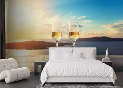 Two champagne glasses on the edge of infinity swimming pool at sunset on Santorini island Wall mural