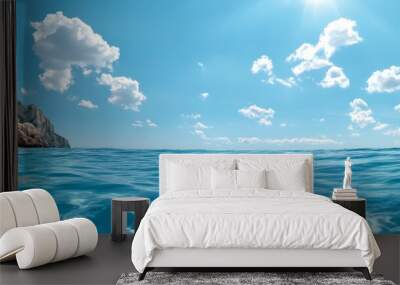 A serene ocean scene with a calm, clear blue surface. The sun shines brightly above, reflecting off the water. The distant coastline adds a touch of depth and serenity to the composition. This image c Wall mural