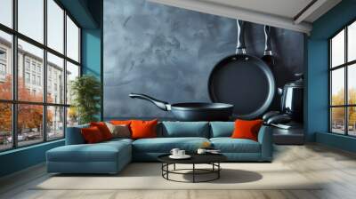 A trio of black frying pans and a black kettle, arranged on a grey background, represent culinary tools, cooking, and kitchen organization. - A trio of black frying pans and a black kettle, arranged o Wall mural