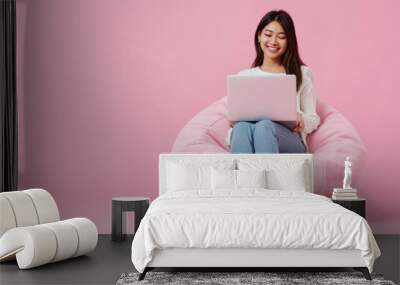 Full body young happy young woman of Asian ethnicity sit in bag chair use work on laptop isolated on plain pink background. AI generative Wall mural