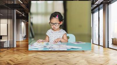 Cute little girl wearing glasses playing jig saw at green table. Wall mural